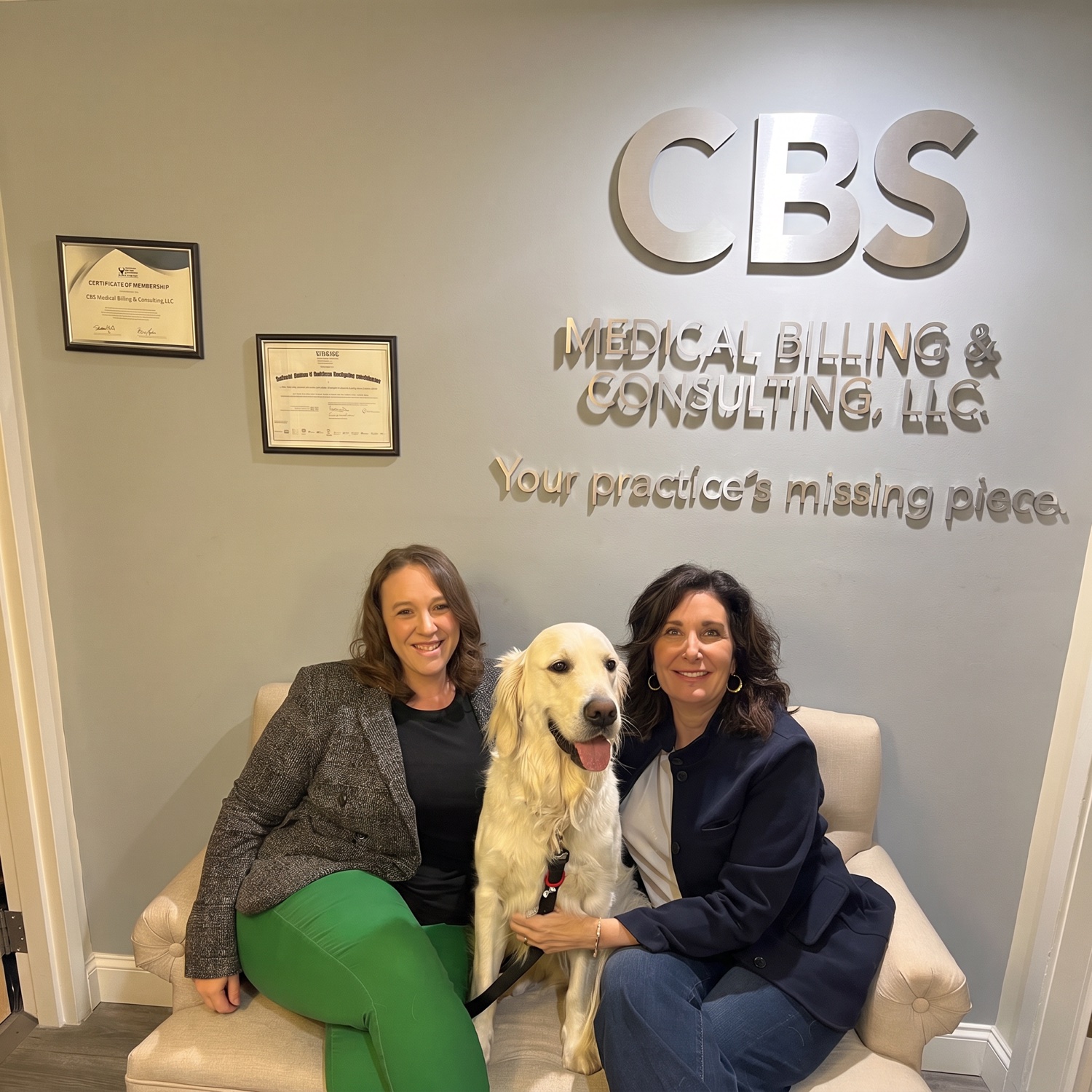 CBS Medical Billing team members Erin and Stacy with office dog Mac beneath the CBS office signage